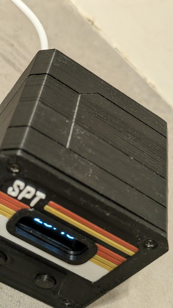 FDM print close-up — layer lines, diagonal seam, four screws holding the faceplate