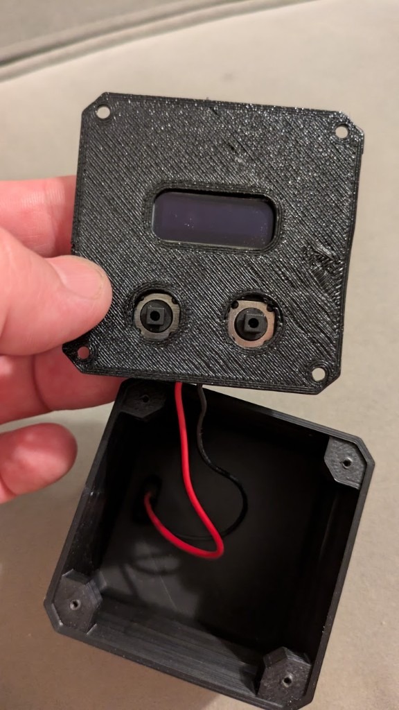 Faceplate lifted off — OLED cutout, two buttons, FDM layer lines in daylight